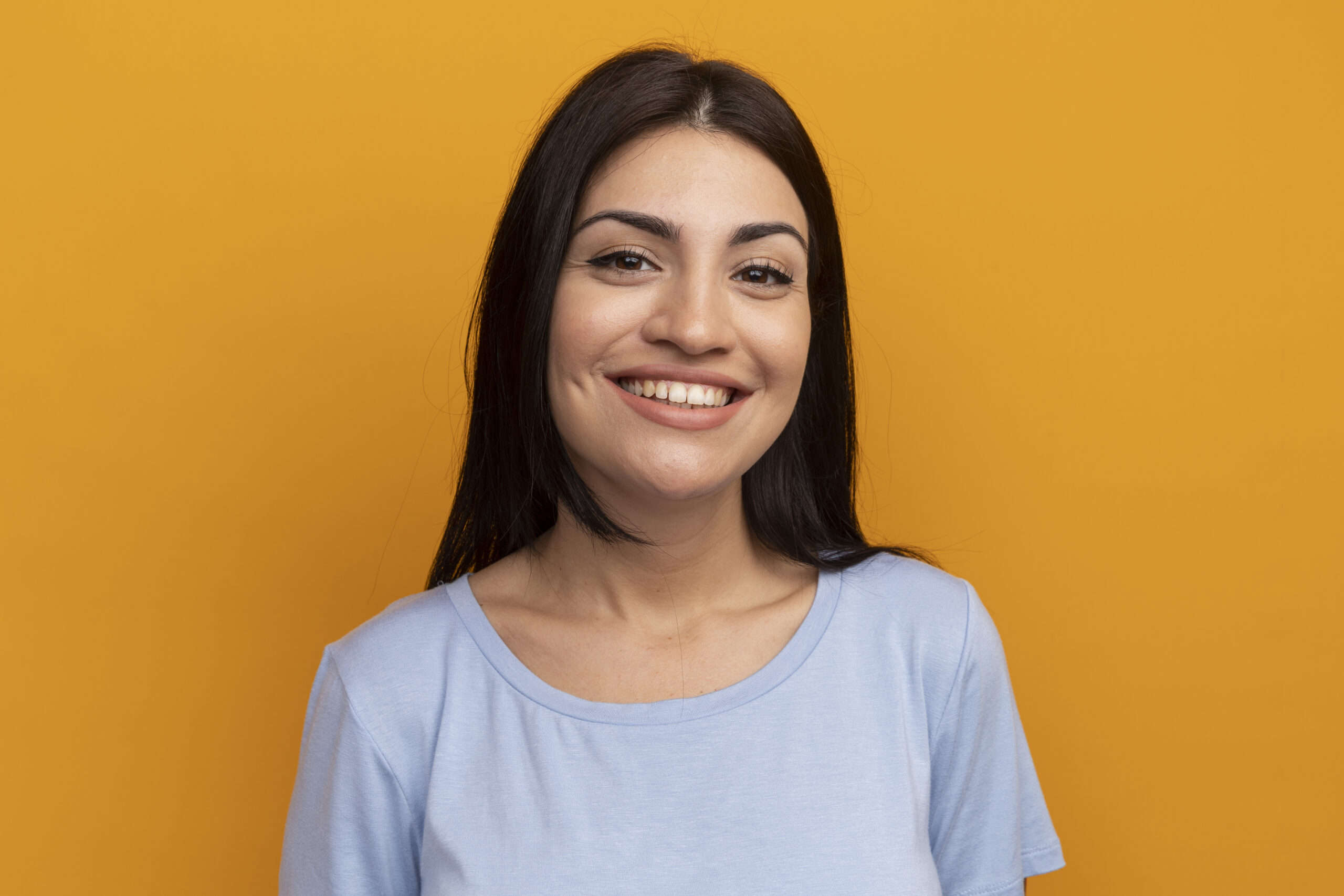 smiling pretty brunette caucasian girl looking at camera isolated on orange background with copy space
