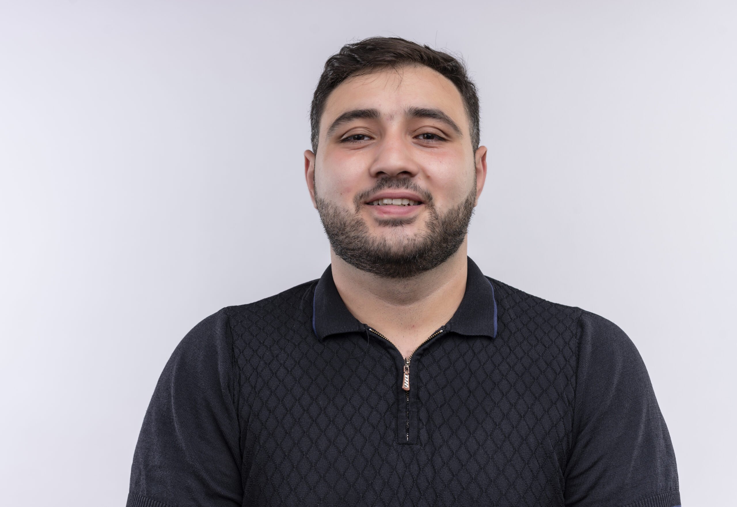 young bearded man in black shirt looking at camera smiling happy and positive standing over white background