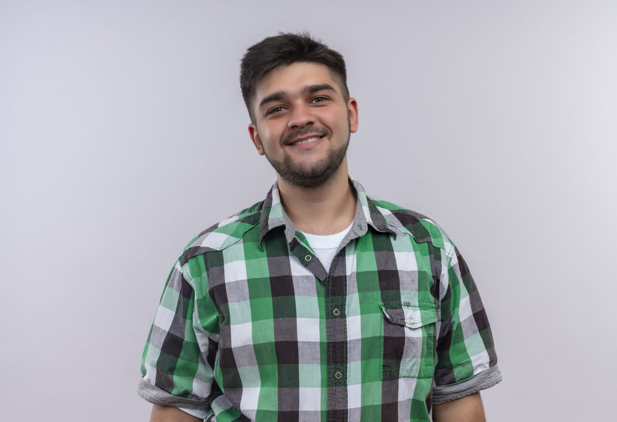 young handsome guy wearing checkered shirt looking happily at camera standing over white background